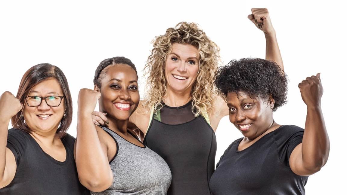 Four mid-life women of different ethnicities grouped together and raising a fist to show strength 