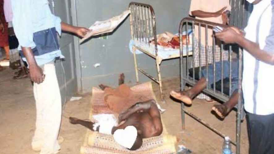 Mityana Hospital, Uganda. A patient lies on the floor surrounded by beds in poor state. 